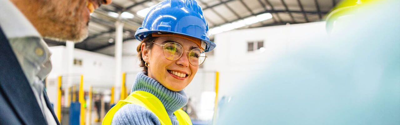 o fata cu casca de muncitor zambeste intr-o fabrica